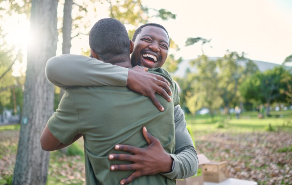 Charity, happy and hug with volunteer friends in a park for community, charity or donation of time